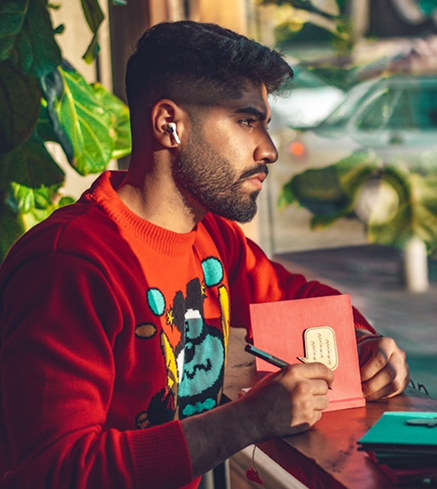 A person wearing wireless earbuds while writing in a notebook